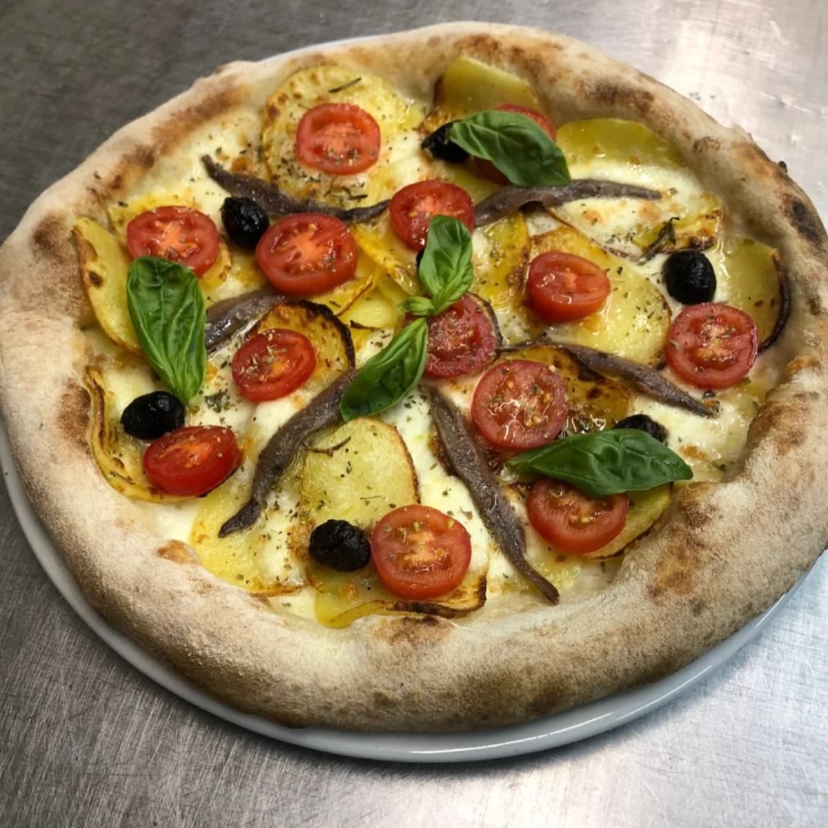 A Pagnotta pizza with potatoes, tomatoes, olives, anchovies, and basil