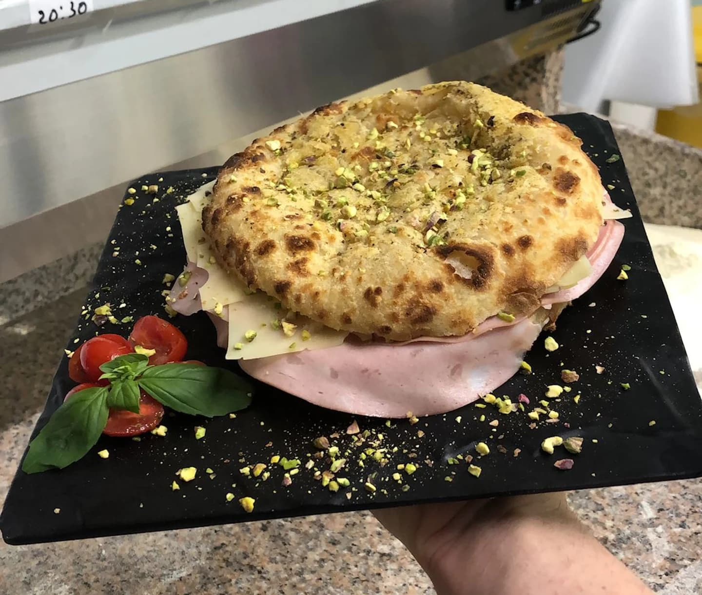 An A Pagnotta sandwich with sliced meat, cheese, pistachios, tomatoes, and basil