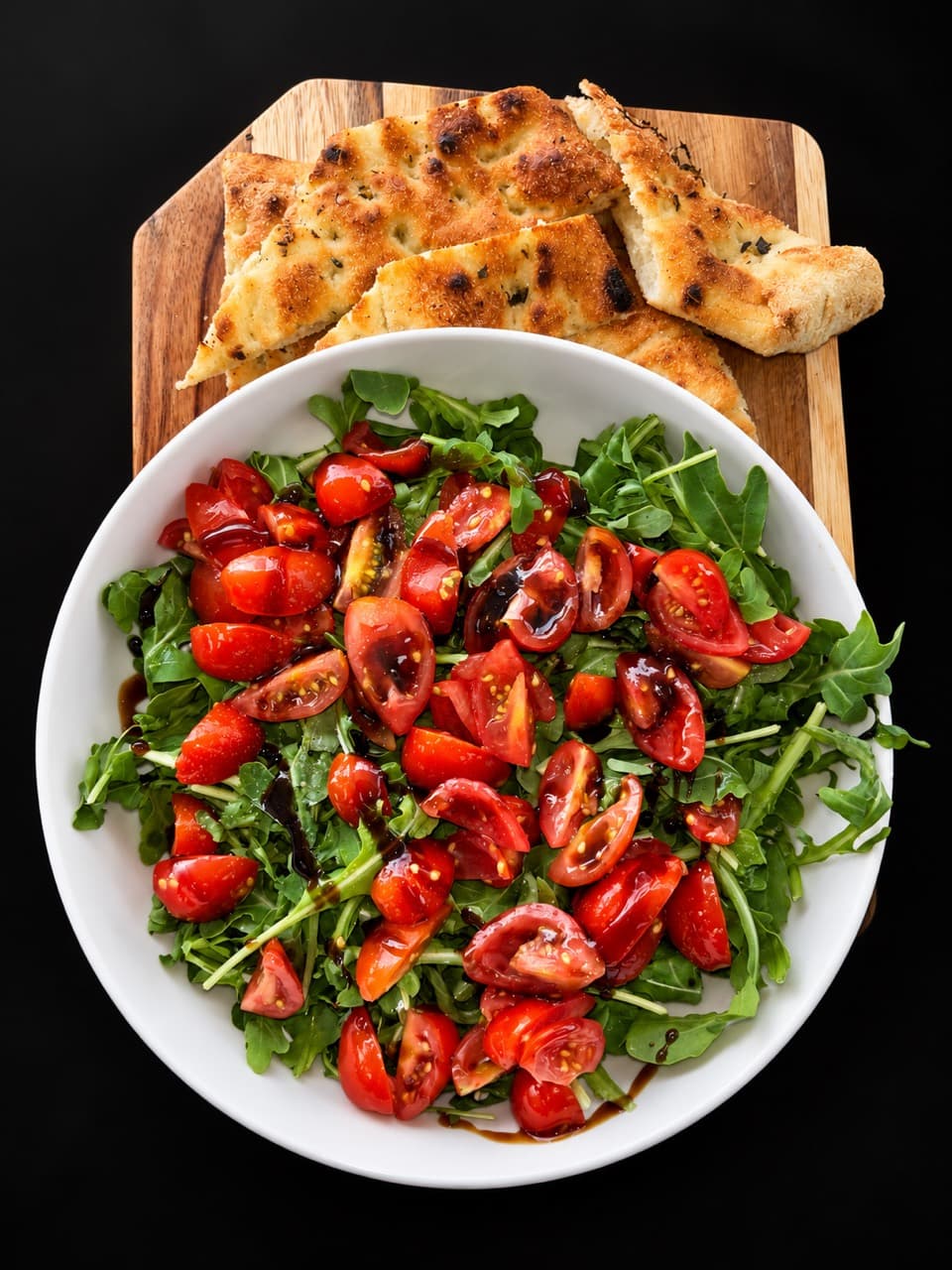 Arugula salad with cherry tomatoes and balsamic glaze in a white bowl