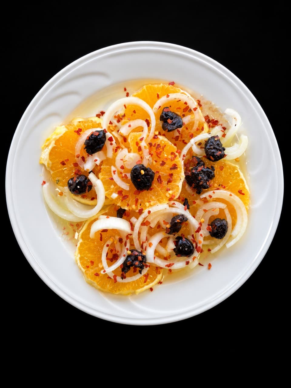 Sicilian salad with sliced oranges, onions, and black olives on a white plate